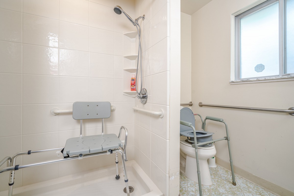 An accessible bathroom featuring a shower with a shower chair and grab bars, alongside a toilet with support rails.