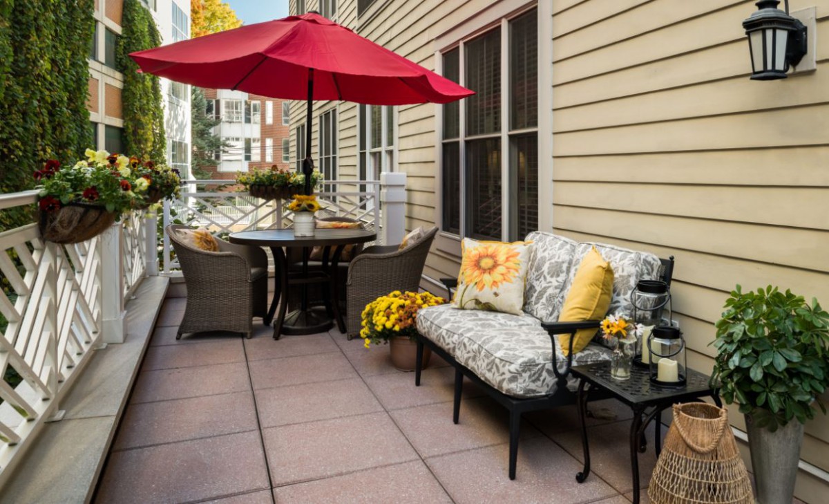 A cozy patio setup with comfortable seating, vibrant cushions, a large umbrella, and decorative flowers.