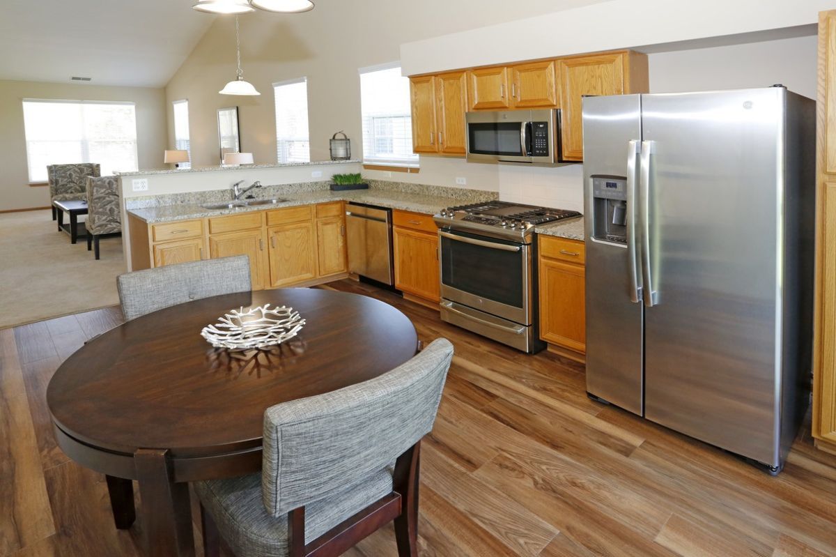A modern kitchen with wooden cabinets, stainless steel appliances, and a dining area.