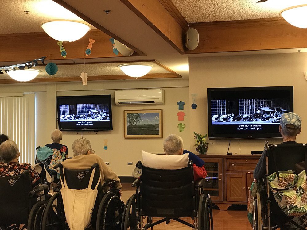 Elderly residents in a nursing home gather to watch television together.