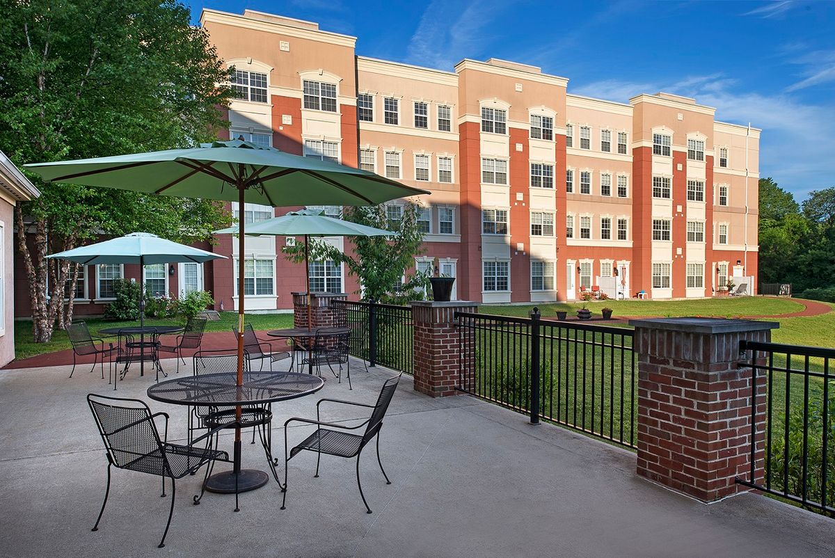 An outdoor patio area with tables and umbrellas in front of a multi-story residential building.