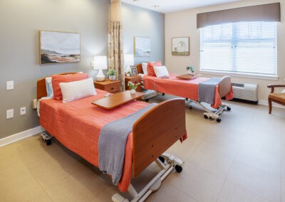 A well-lit hospital room with two neatly made beds and bedside tables.