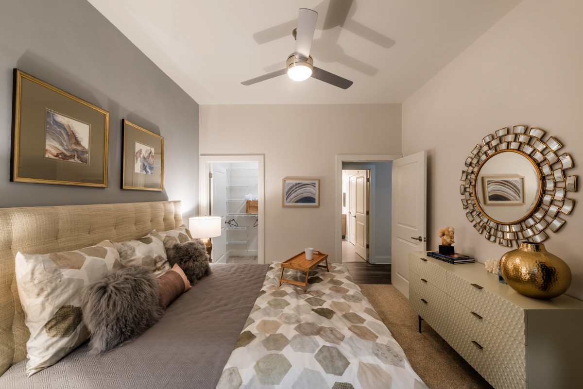 A cozy bedroom with neutral tones, featuring a ceiling fan, artwork, and a neatly arranged dresser.