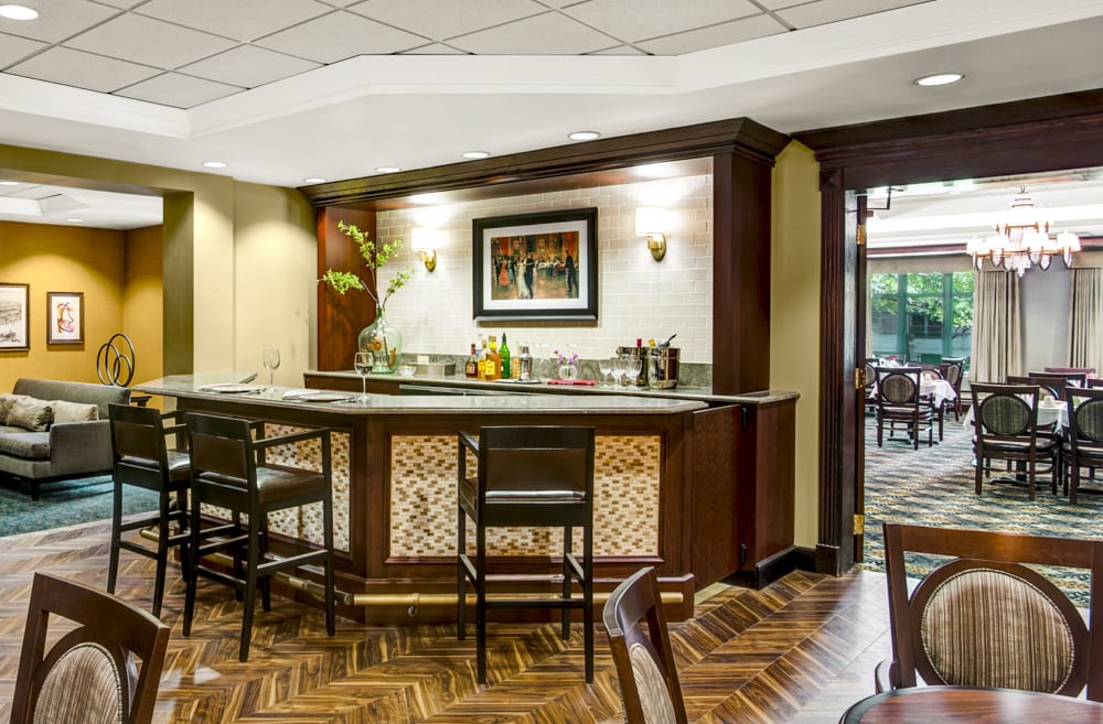A cozy bar area with a wooden counter and chairs, stylish lighting, and decorative elements.