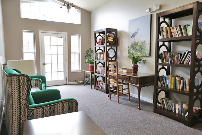 A cozy living room with bookshelves, a desk, and bright natural lighting.