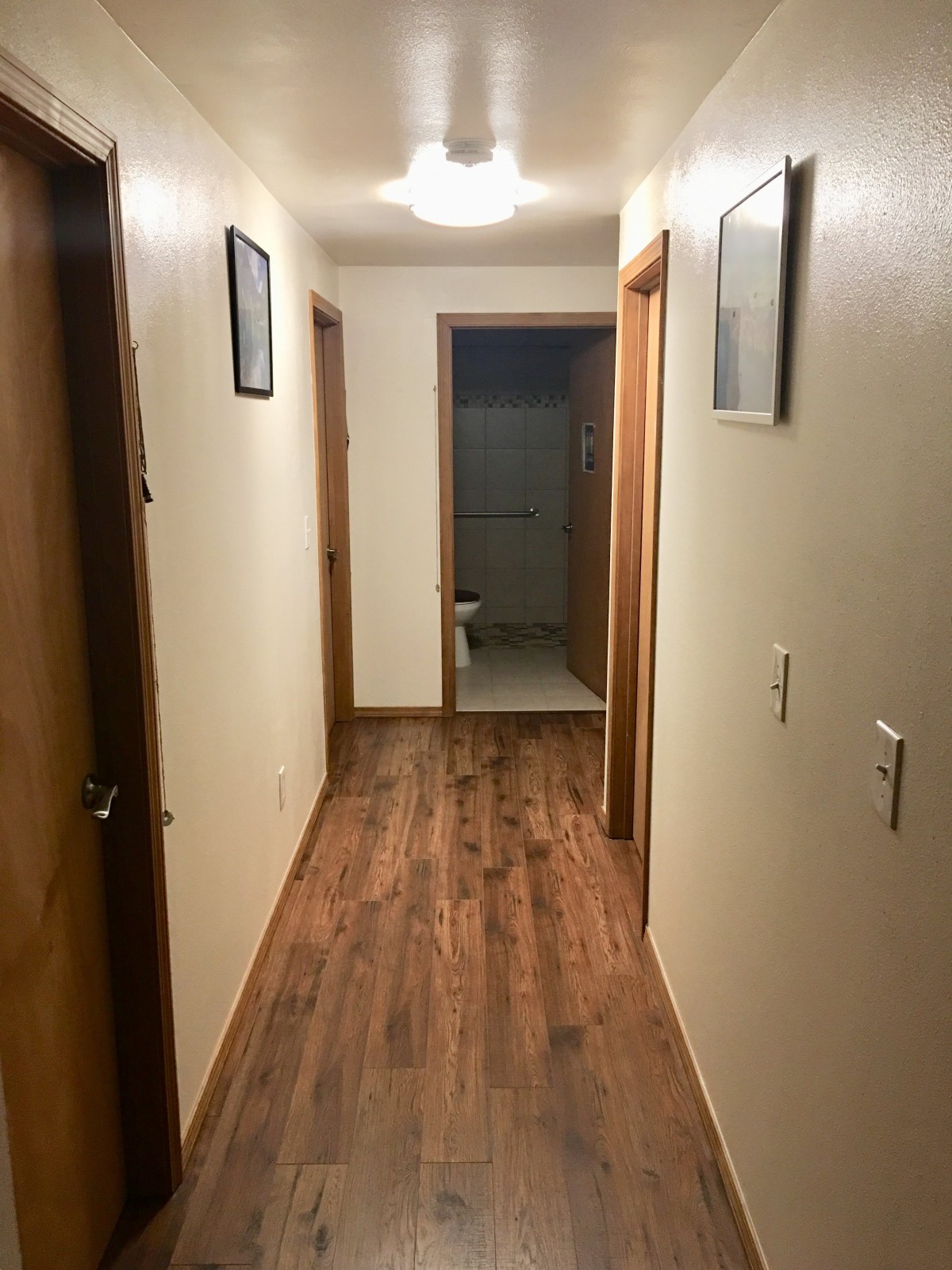 A hallway with wooden floors leading to a bathroom.