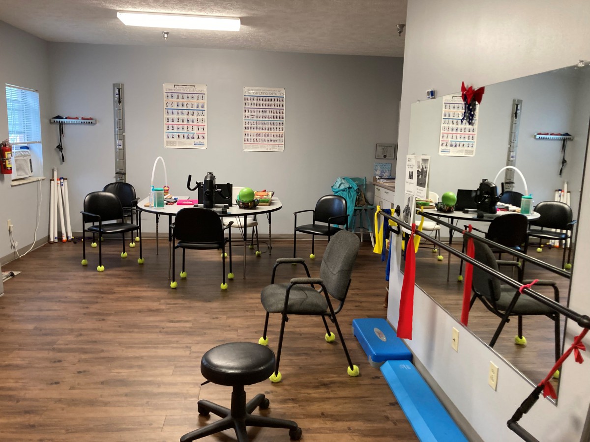 A physical therapy room equipped with chairs, exercise equipment, and mirrors.