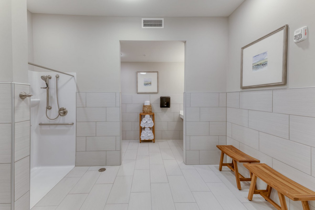 A spacious bathroom with a walk-in shower, neatly folded towels on a wooden rack, and a bench for seating.