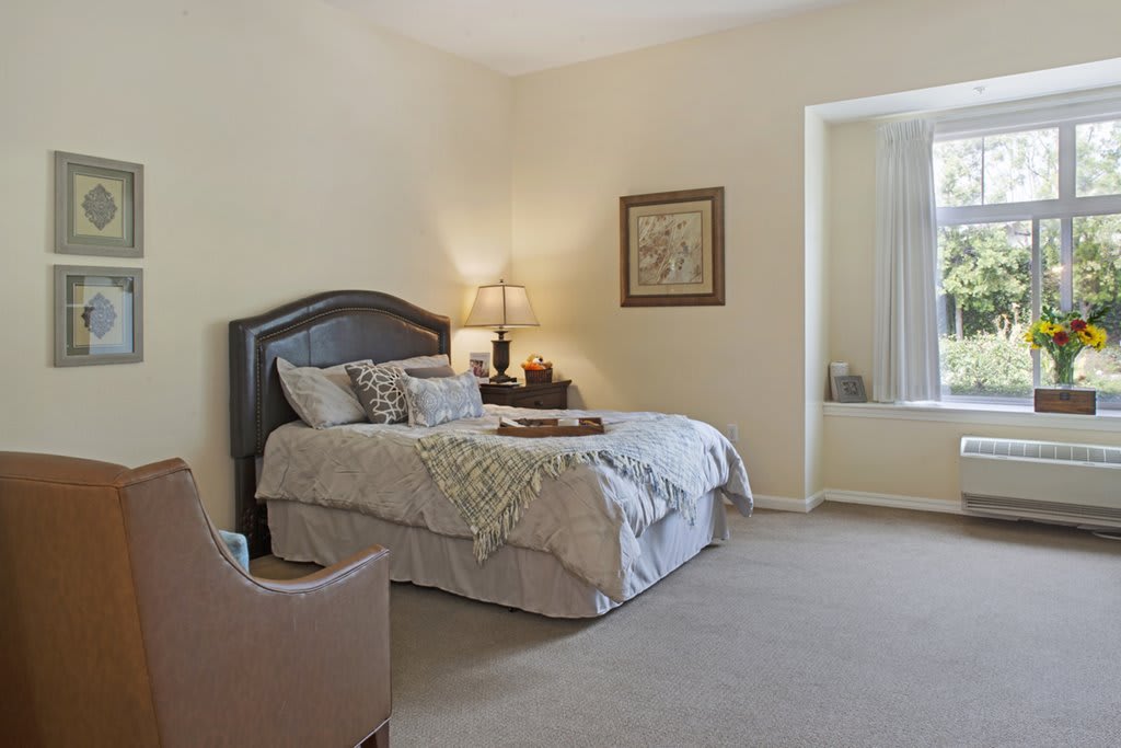 A cozy bedroom with a neatly made bed, a nightstand with a lamp, and tasteful decor.