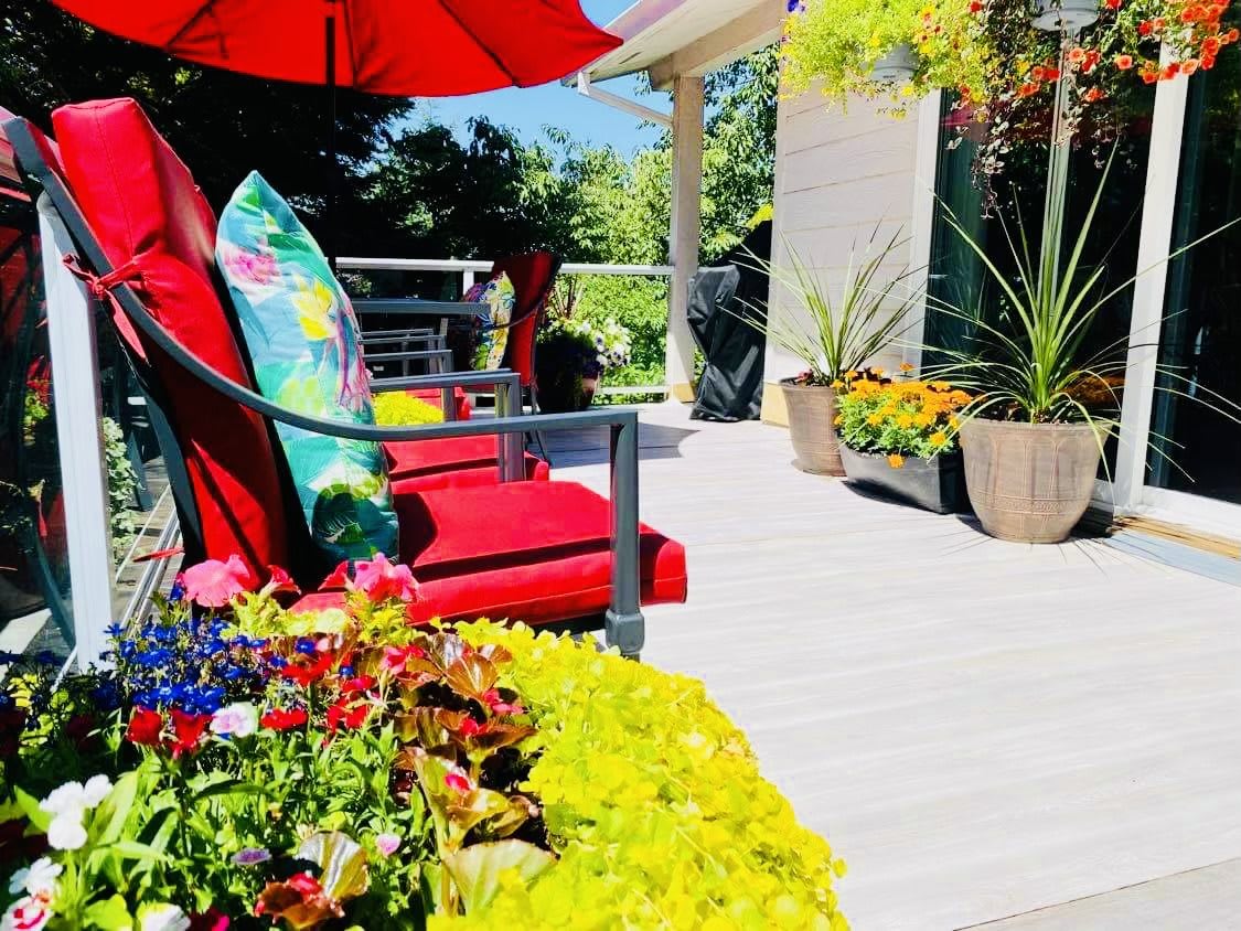 A vibrant patio setting with colorful cushions, flowers, and a red umbrella on a sunny day.