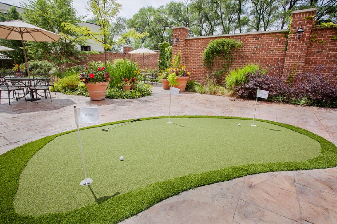 A backyard featuring a well-maintained putting green surrounded by lush garden landscaping.