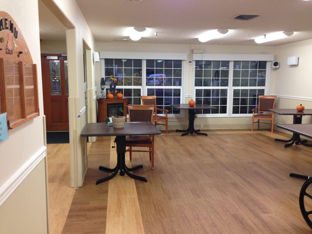 An empty room with tables and chairs, featuring large windows and wooden flooring.