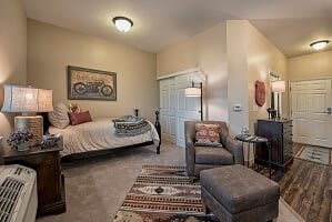 A cozy bedroom with warm decor, featuring a bed, armchair, and an art piece on the wall.