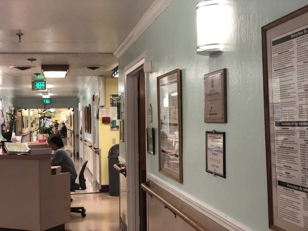 A hospital hallway with a nursing station and framed certificates on the wall.