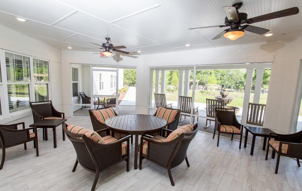 A spacious, bright interior patio with round tables and chairs, surrounded by large windows overlooking greenery.