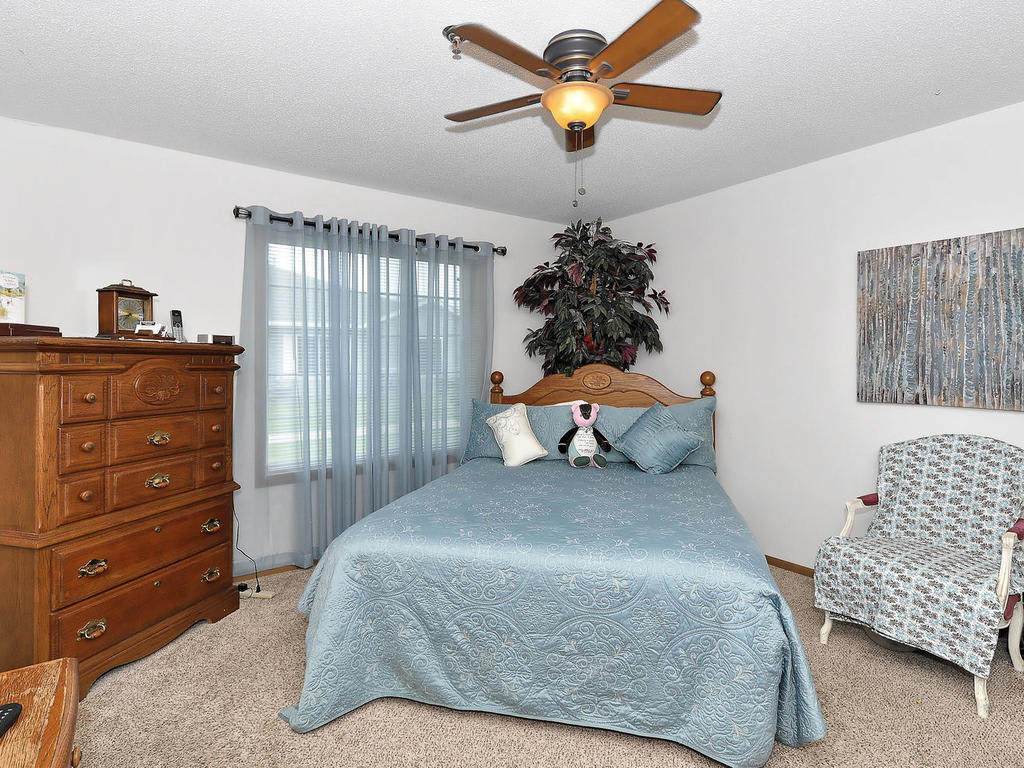 A cozy bedroom with a blue bedspread, ceiling fan, and wooden dresser.