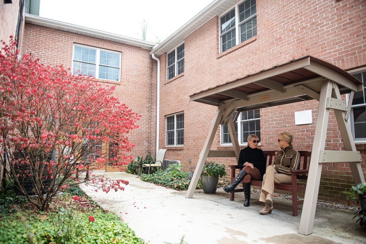 Two people sitting on a bench in an outdoor garden area beside a brick building.