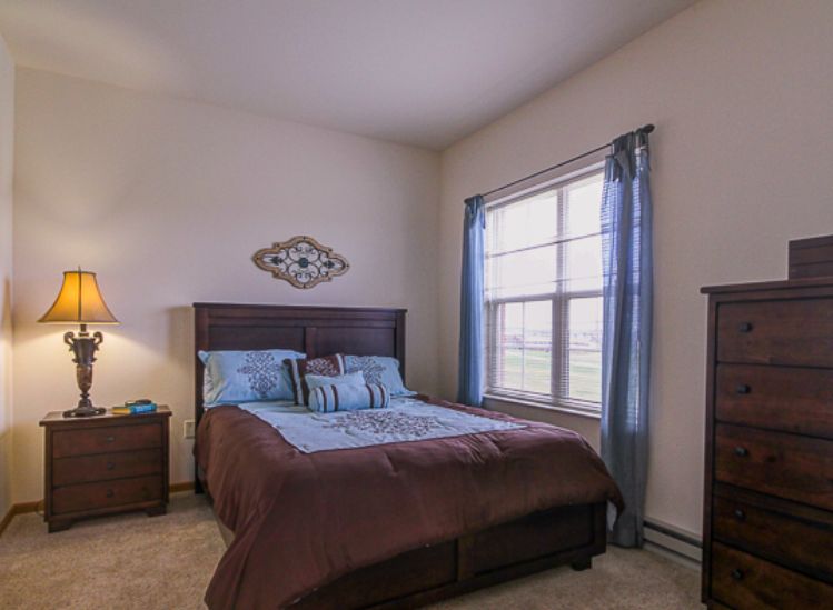 A cozy bedroom with a neatly made bed, wooden furniture, and natural light filtering through the window.