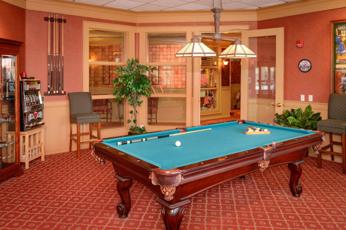 A cozy billiards room featuring a pool table with green felt, classic wood furniture, and warm lighting.