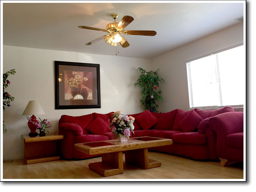 A cozy living room with a red sofa set, wooden coffee table, and ceiling fan.