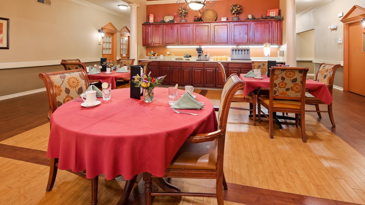 A cozy restaurant dining area with tables set for a meal, featuring red tablecloths and elegant decor.