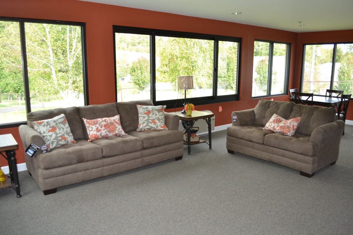 A spacious living room featuring two gray sofas, large windows with abundant natural light, and a cozy carpeted floor.
