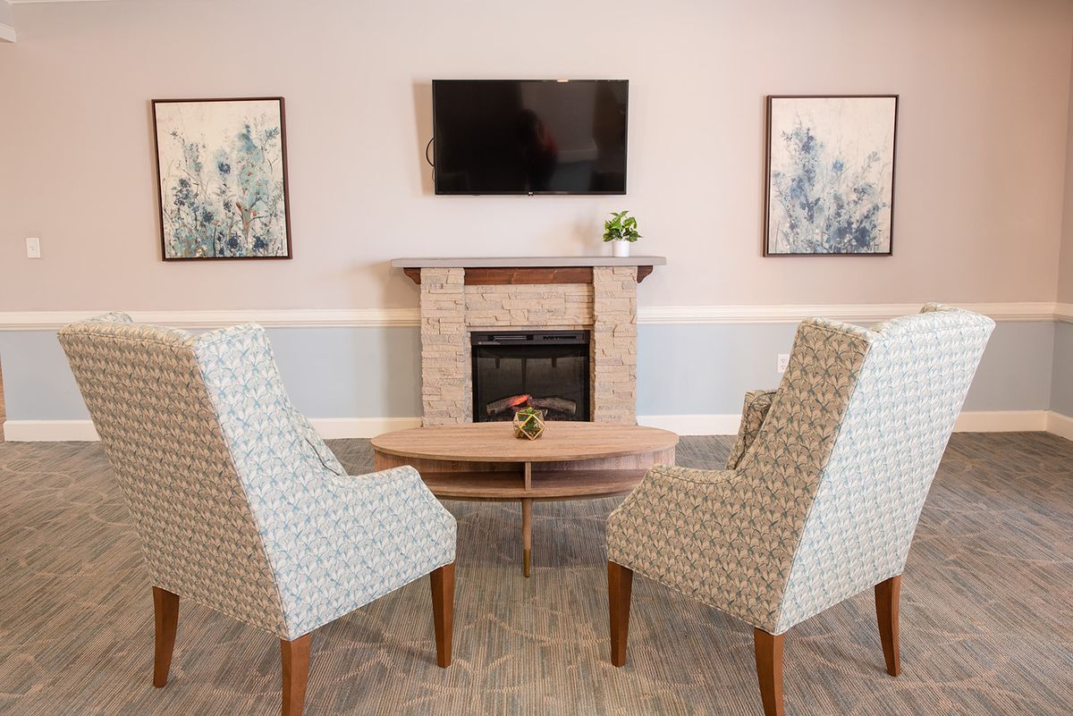 A cozy living room setup with patterned chairs and a television above the fireplace.
