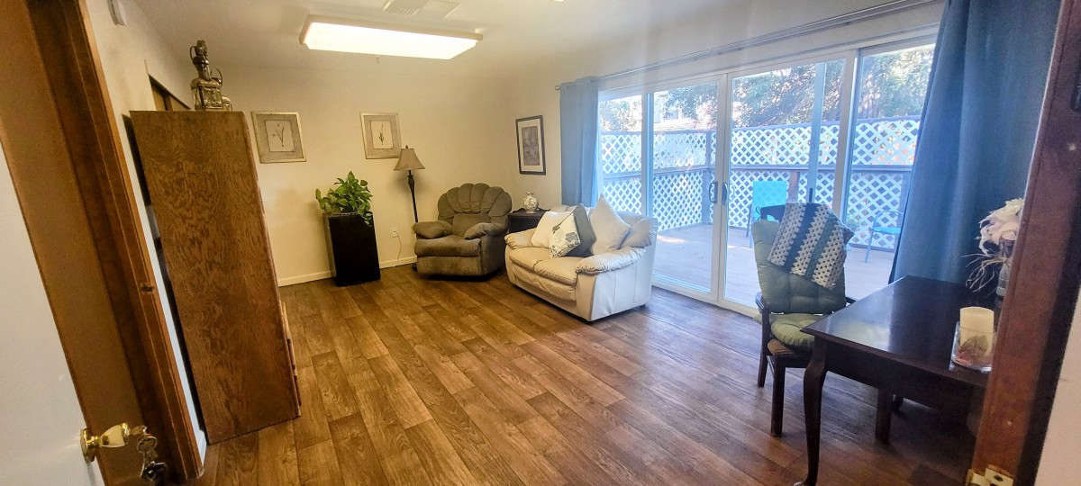 A cozy living room with a sofa, armchair, and wooden flooring, featuring a sliding door that leads outside.