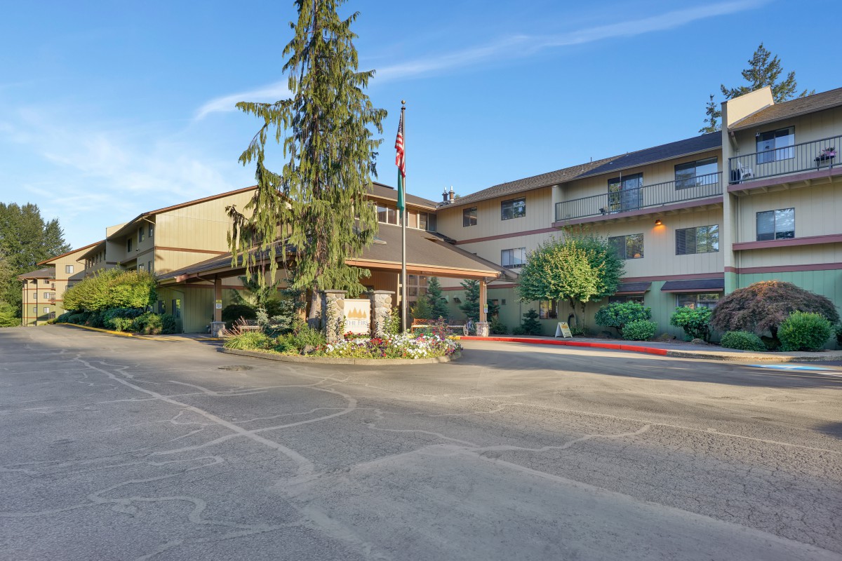 The exterior of a hotel building with an entrance surrounded by trees and a clear sky.