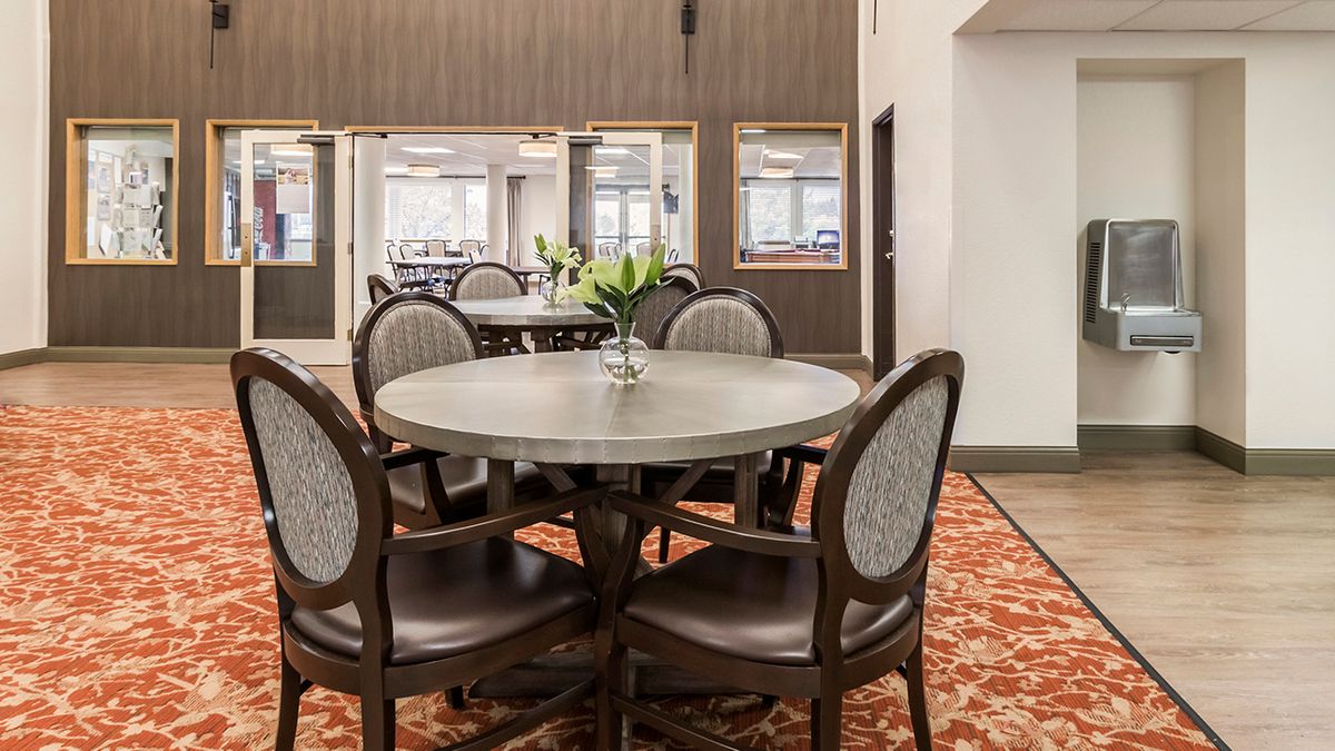 A cozy dining area featuring a round table surrounded by chairs, adorned with a vase of flowers on a patterned carpet.