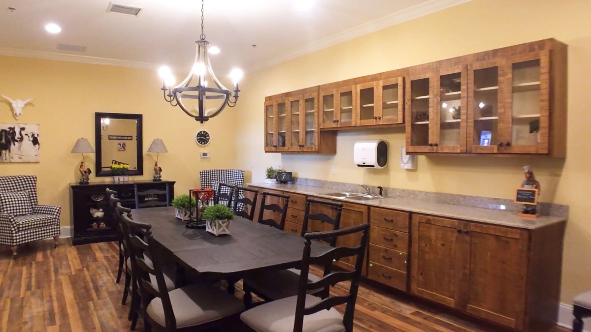 A cozy dining area with a wooden table and chairs, illuminated by a chandelier, adjacent to a kitchen space with wooden cabinets.