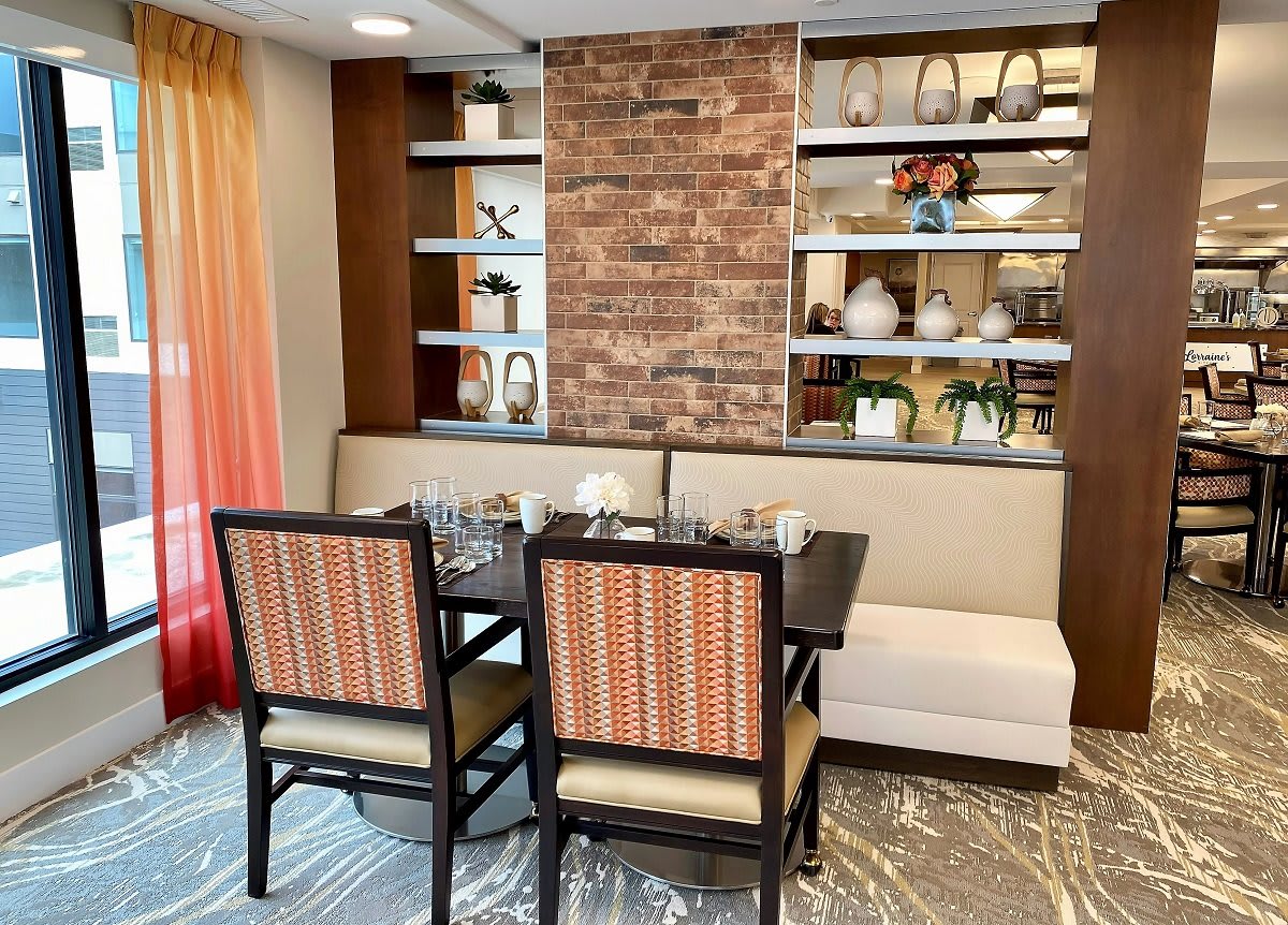 A modern dining area with elegant seating and decorative shelving, featuring a brick accent wall.