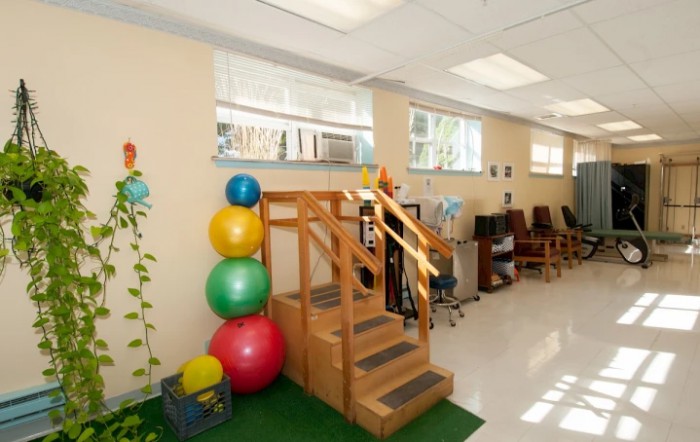 A brightly lit therapy room equipped with exercise balls and rehabilitation stairs.