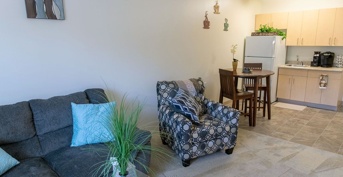 A cozy living room with a patterned armchair and sofa, adjacent to a dining area.