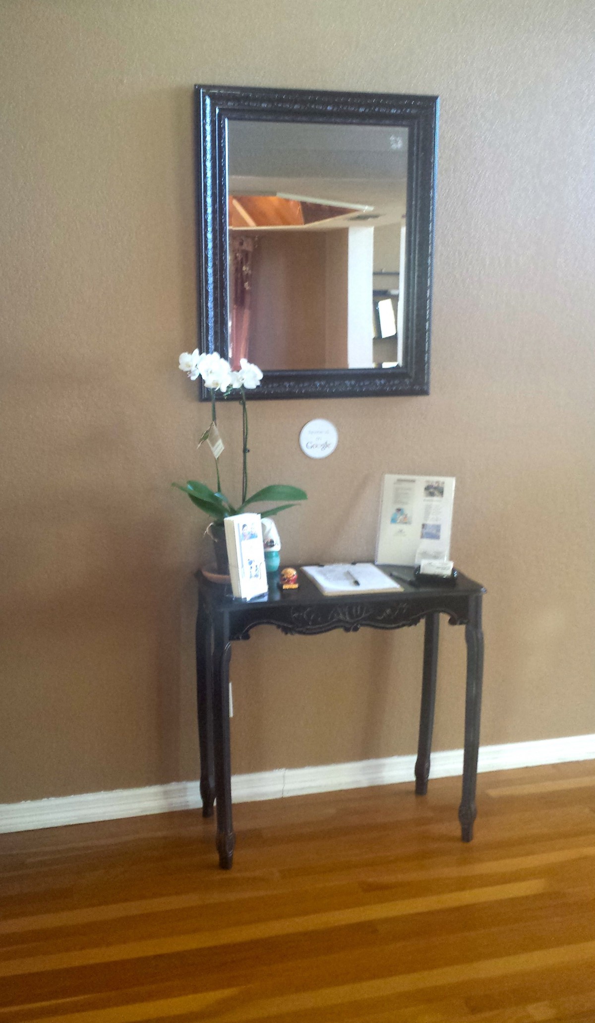 A small black table with decorative items and an orchid sits below a wall-mounted mirror.