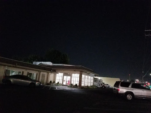 A nighttime view of a building with illuminated windows and parked cars in the foreground.