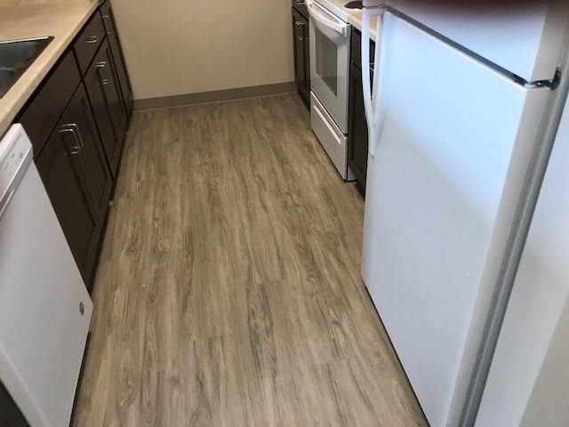 A modern kitchen with wooden flooring and appliances.