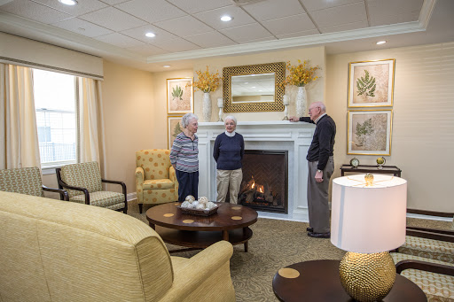 A cozy living room where two seniors engage in conversation while standing near a fireplace.