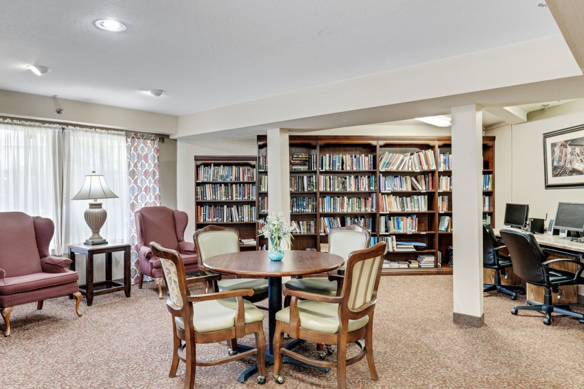 A cozy library with bookshelves, a round table, and comfortable chairs for reading.