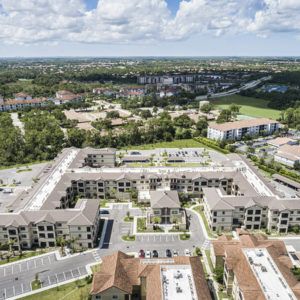 Aerial view of a suburban apartment complex with surrounding greenery and roads.