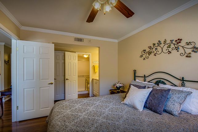 A cozy bedroom with a neatly made bed, ceiling fan, and stylish decor.
