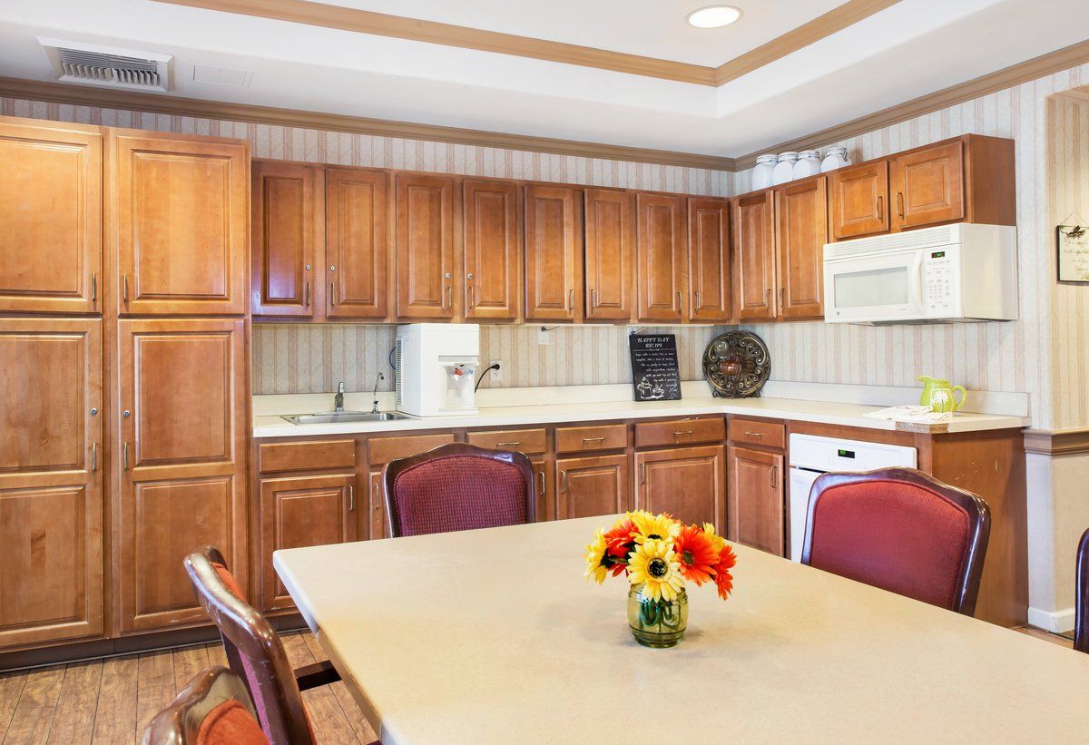 A warm kitchen with wooden cabinets and a dining area adorned with a flower vase.