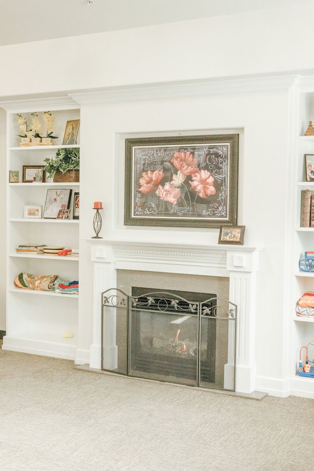A cozy living room featuring a fireplace with decorative shelves, adorned with artwork and books.