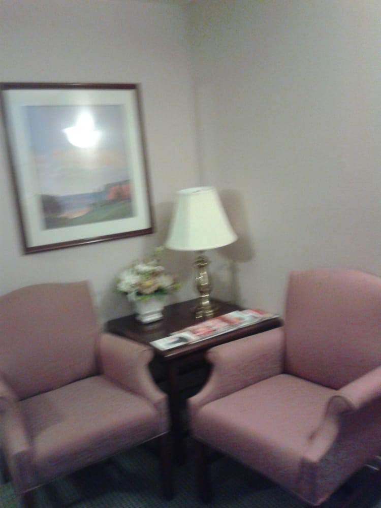 A cozy waiting room with chairs, a table, and a lamp.