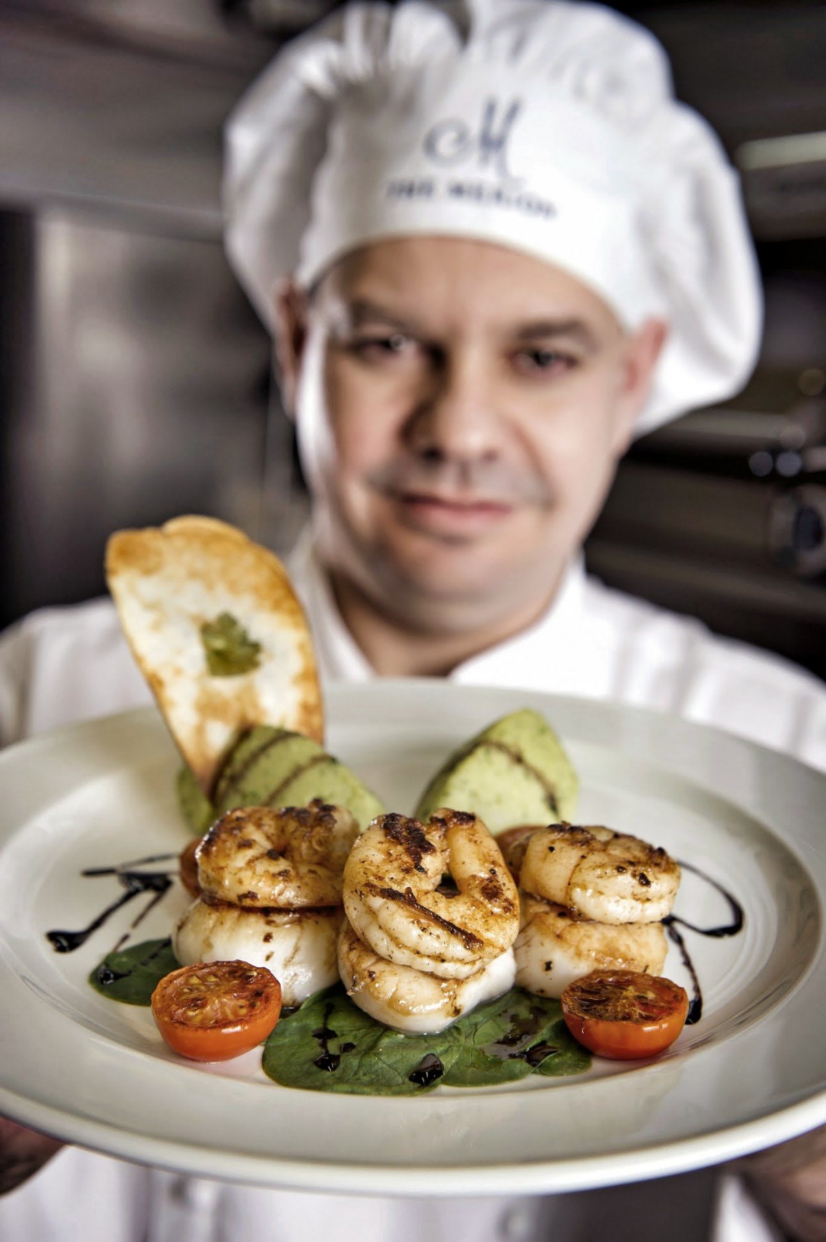 A chef presenting a beautifully plated dish of shrimp and vegetables.