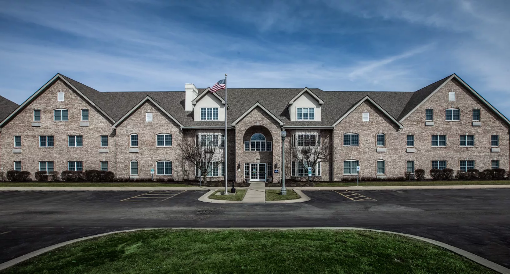 A symmetrical brick residential building with a flagpole in front and a parking lot.
