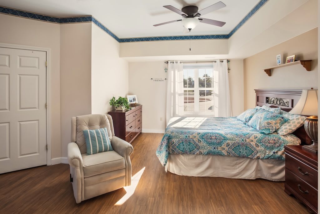 A cozy bedroom featuring a comfortable bed, armchair, and natural lighting from a large window.