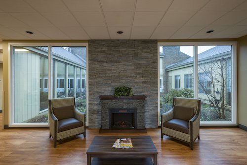 A modern living room with a stone fireplace, two chairs, and large windows.