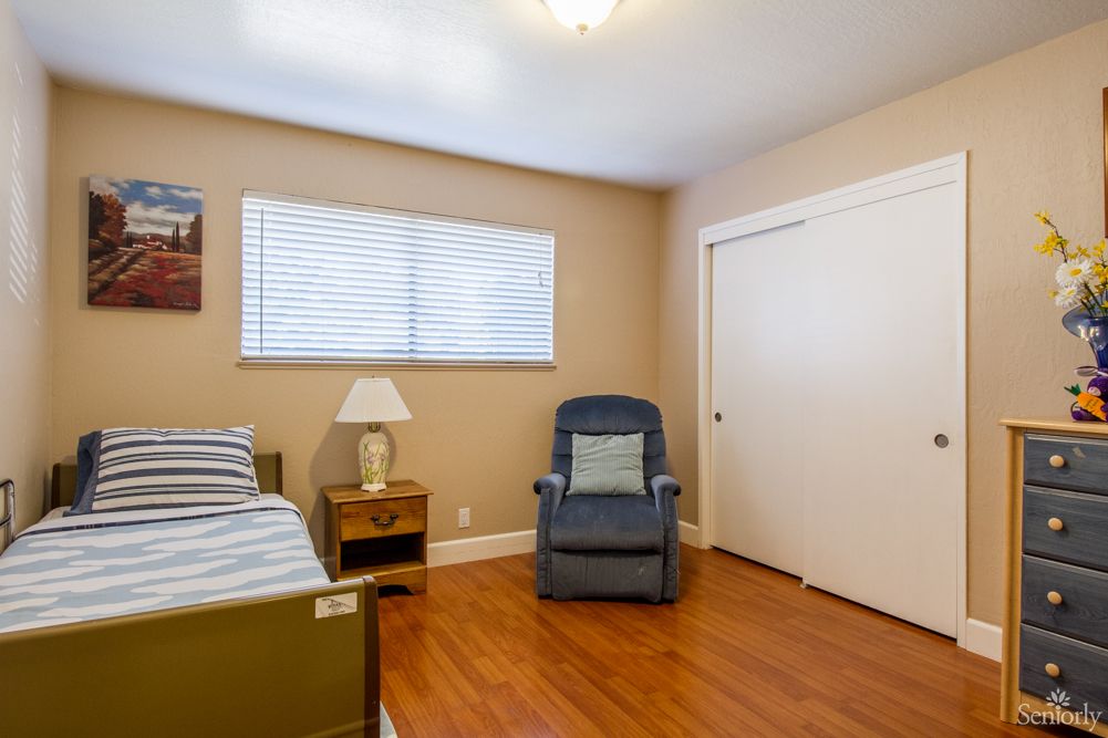 A cozy bedroom with a bed, armchair, and wooden flooring.