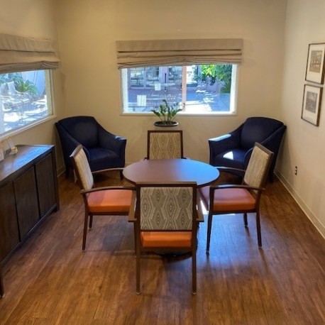 A cozy room featuring a round table surrounded by four chairs, two comfortable armchairs, and ample natural light from the windows.